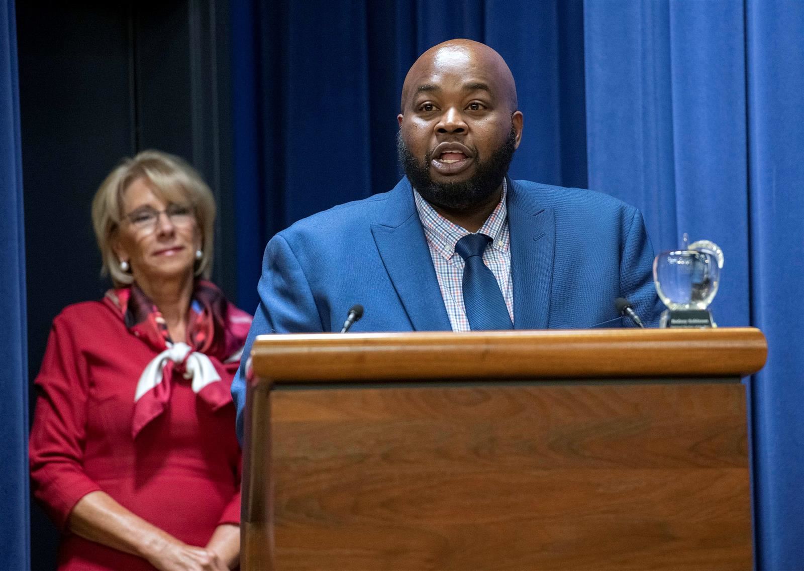 U.S. Secretary of Education Betsy DeVos listens as 2019 Teacher of the Year Rodney Robinson accepts his award.  